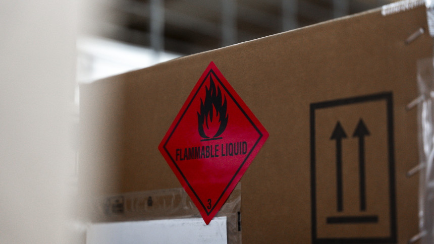 Nahaufnahme eines Kartons mit einem roten Gefahrensymbol für entzündbare Flüssigkeiten und einem schwarzen Symbol mit zwei nach oben zeigenden Pfeilen