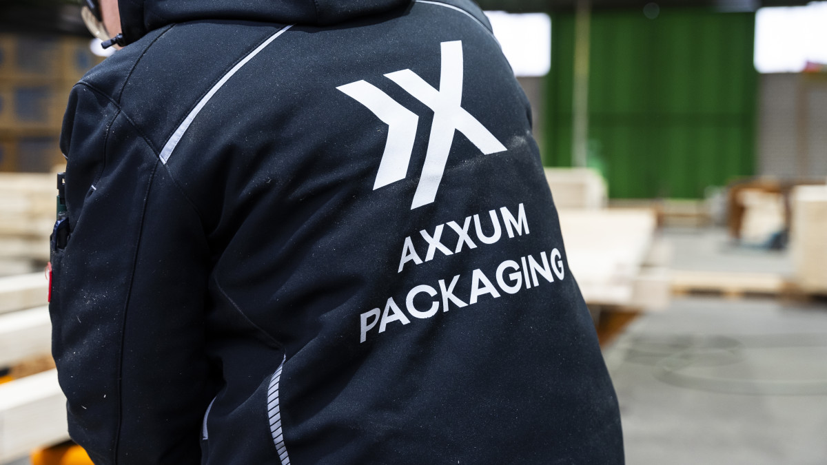 Rückenansicht einer Person in Arbeitsjacke mit dem Schriftzug AXXUM PACKAGING in einer Lagerhalle