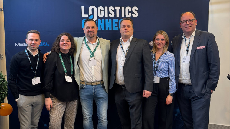 Sechs Personen stehen vor einem blauen Messestand mit der Aufschrift LOGISTICS CONNECT