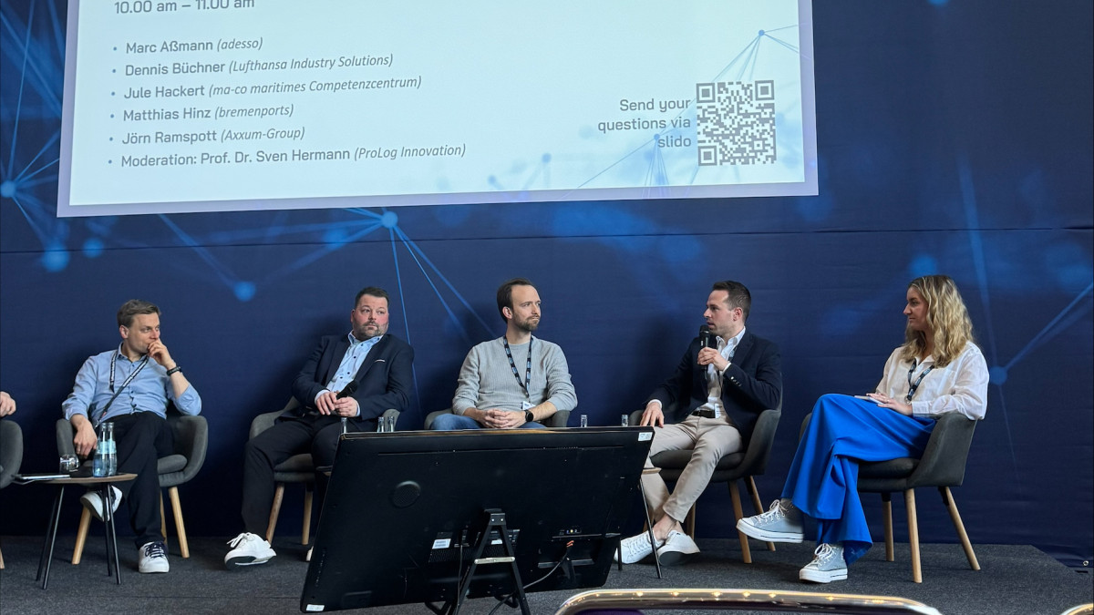 Podiumsdiskussion mit mehreren Personen vor Publikum in einem Konferenzsaal mit großem Bildschirm und Banner LOGISTICS CONNECT