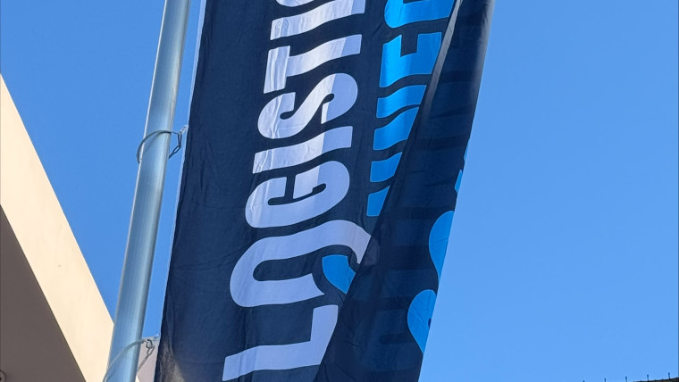Fahne mit weißer und blauer Schrift 'LOGISTICS CONNECT' an Fahnenmast vor blauem Himmel und Gebäudeteil