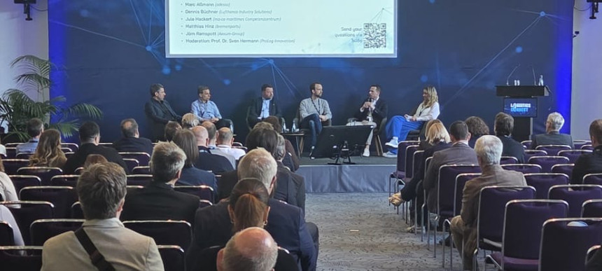 Podiumsdiskussion mit mehreren Personen vor Publikum in einem Konferenzsaal mit großem Bildschirm und Banner LOGISTICS CONNECT