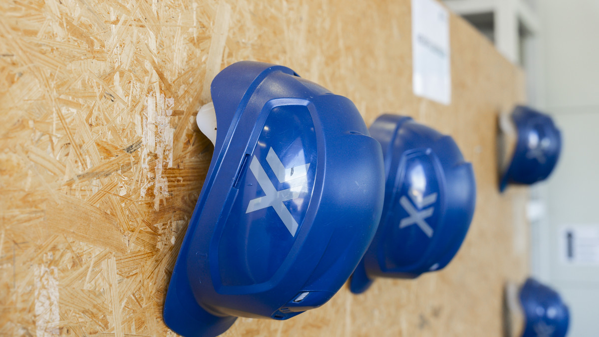 Blaue Schutzhelme mit weißen Logos hängen ordentlich an einer Holzwand.