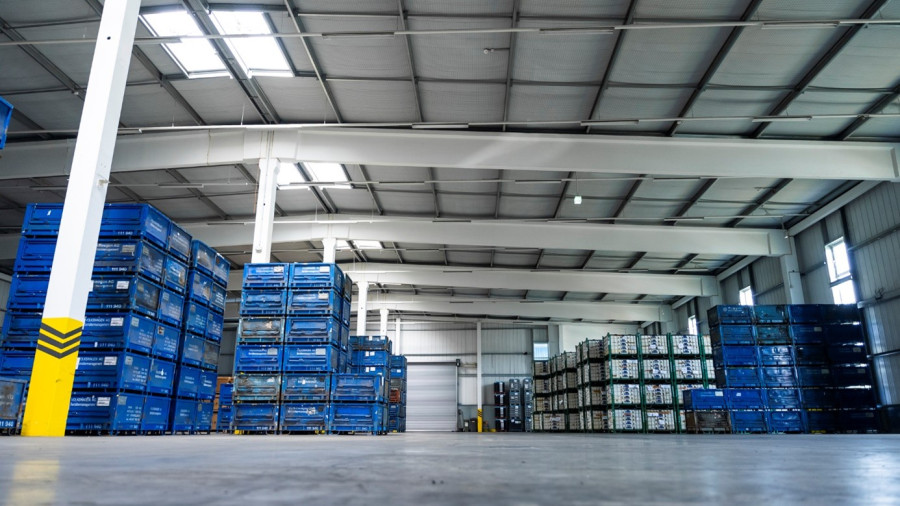 Geräumiges Lagerinnere mit bis zur Decke reichenden Stapeln blauer Kisten, großen Oberlichtern und einem polierten Betonboden.