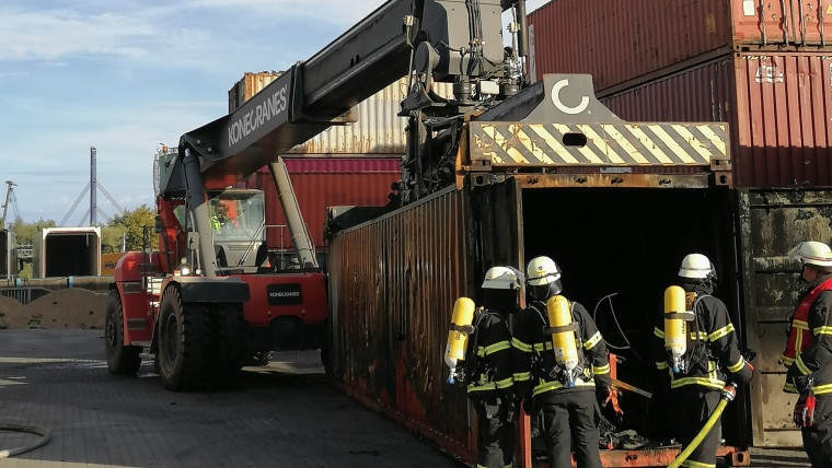 Nach den Explosionen in einer Lagerhalle an der Müggenburger Straße untersuchen Feuerwehrleute in Schutzkleidung mit einem Schlauch einen verkohlten Schiffscontainer