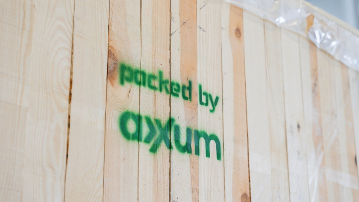 Holzkiste mit vertikalen Brettern, mit grünem Schablonentext „packed by AXXUM“