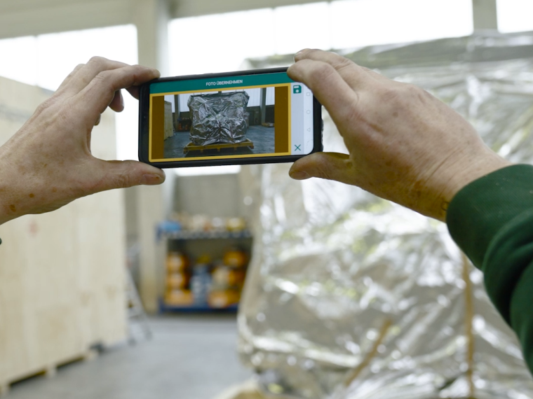 Jemand hält ein  Handy in der Hand und fotografiert eine Großverpackung