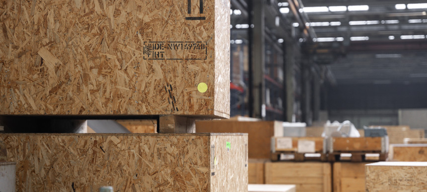 Große Holzverpackungskisten gestapelt in einer Lagerhalle mit sichtbaren Aufklebern und Markierungen