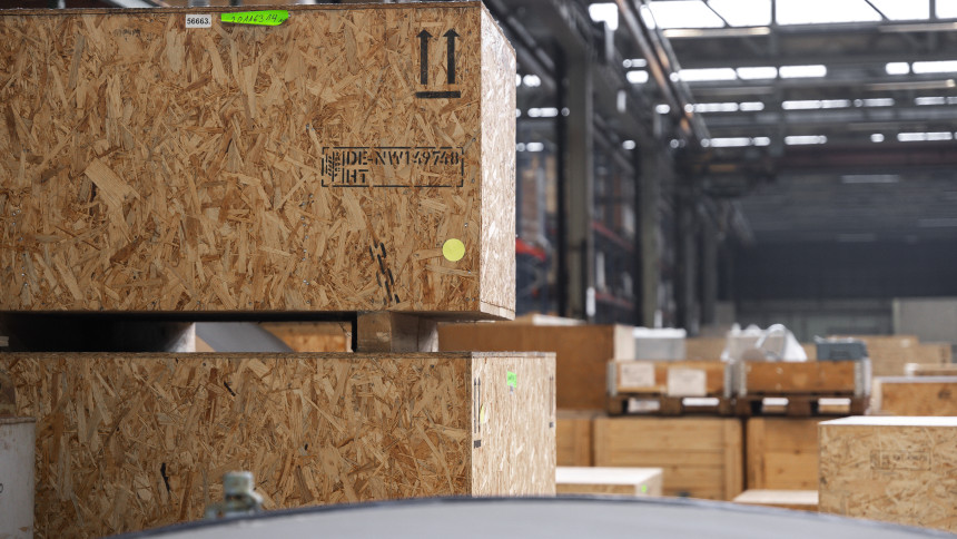 Große Holzverpackungskisten gestapelt in einer Lagerhalle mit sichtbaren Aufklebern und Markierungen