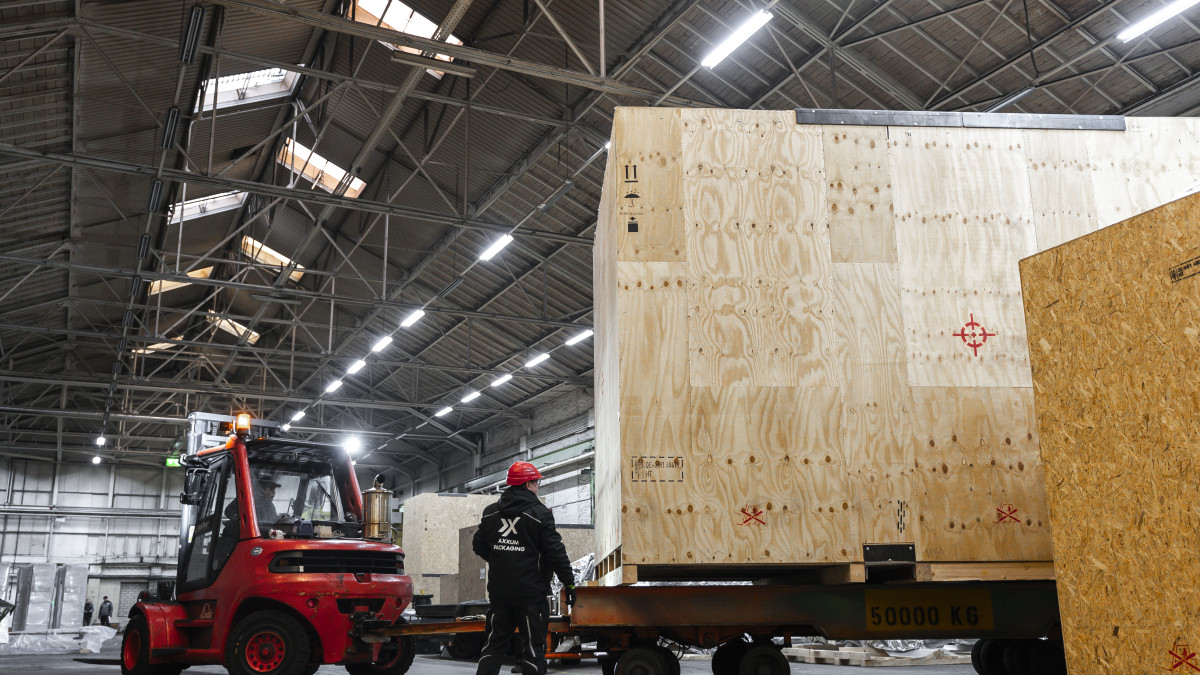 Gabelstapler hebt große Holzverpackung in Lagerhalle mit Arbeiter in Schutzhelm daneben