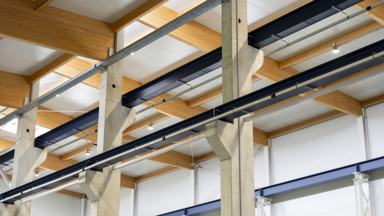 Innenansicht eines großen Lagerhauses mit sichtbaren Holzträgern und Metallrohren.