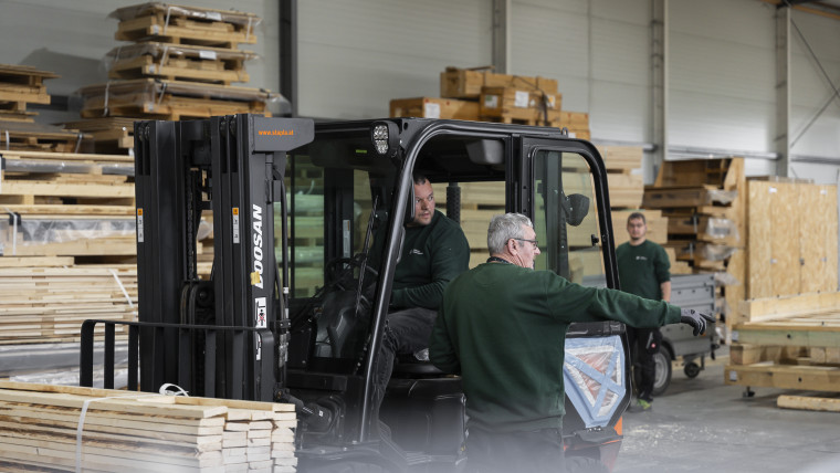Ein Gabelstaplerfahrer und ein Kollege in einem Lager, während sie an einer Aufgabe arbeiten.