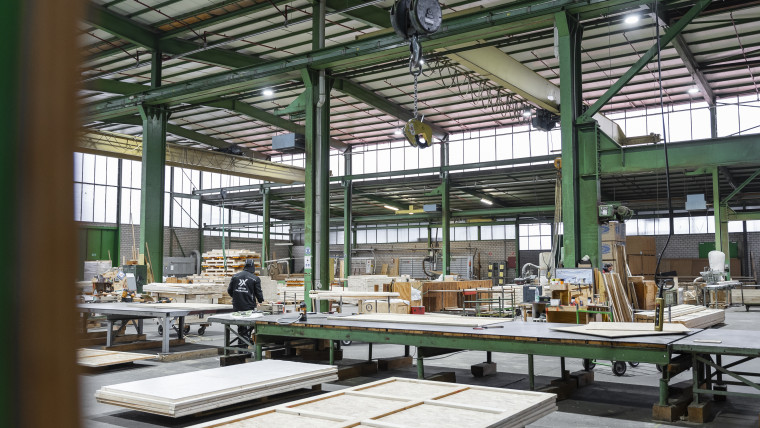 Innenansicht einer Fabrik, in der Holz- und Metallverarbeitung stattfindet, mit Werkzeugen und Materialien sichtbar.