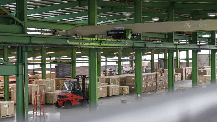 In einem Lagerhaus ist ein Gabelstapler umgeben von Kisten und Paletten.