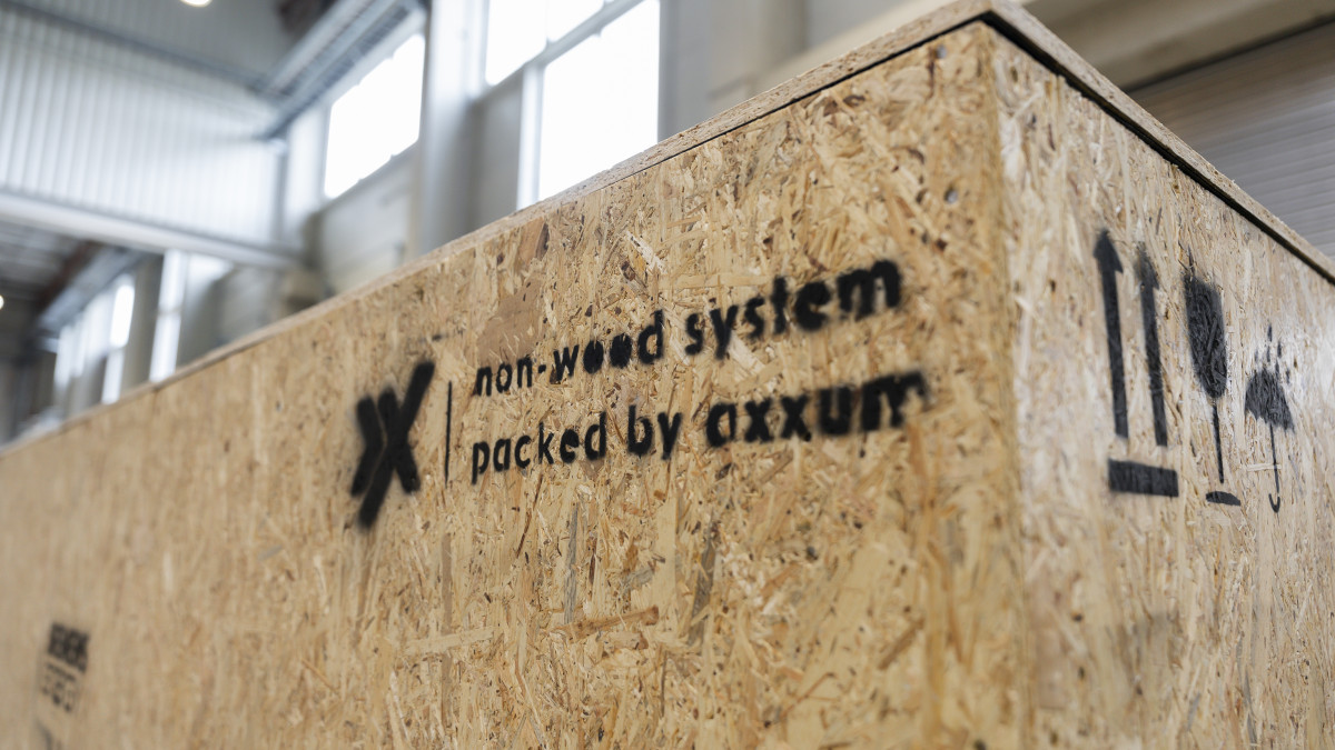 Nahaufnahme einer großen, strukturierten Kiste aus einem nicht aus Holz bestehenden Material in einem Lagerhaus. Auf der Seite ist der Text „non-wood system packed by axxum” aufgedruckt.